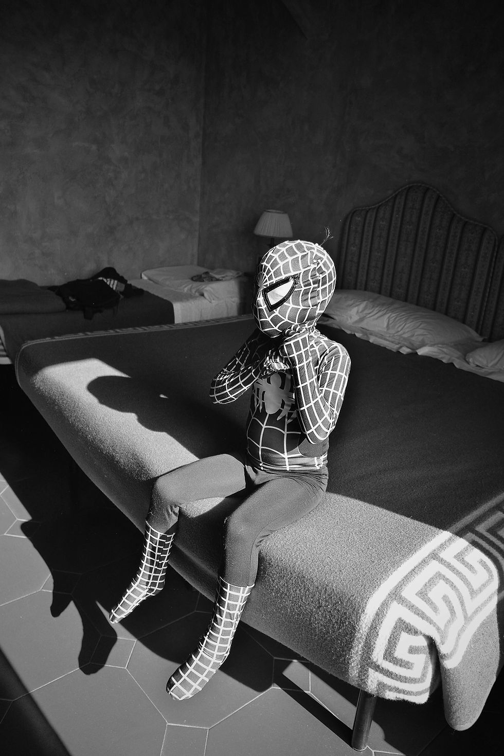 This is a striking black and white photograph that captures a young person dressed in a full Spider-Man costume, including the mask.