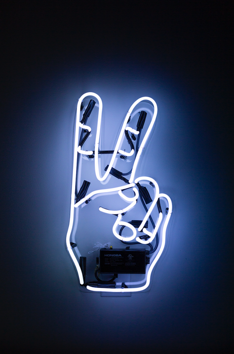 Neon sign shaped like a hand making the peace sign (V sign) glowing with bright white light against a dark background.