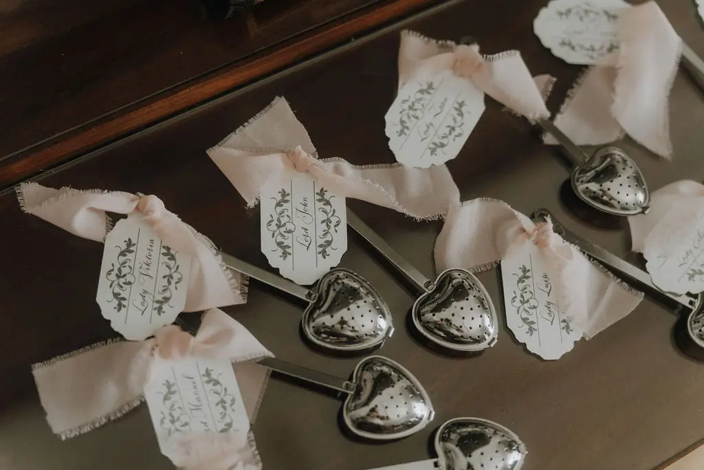 Teesieb als Gastgeschenk mit personalisierten Anhängern und zartrosa Chiffonband