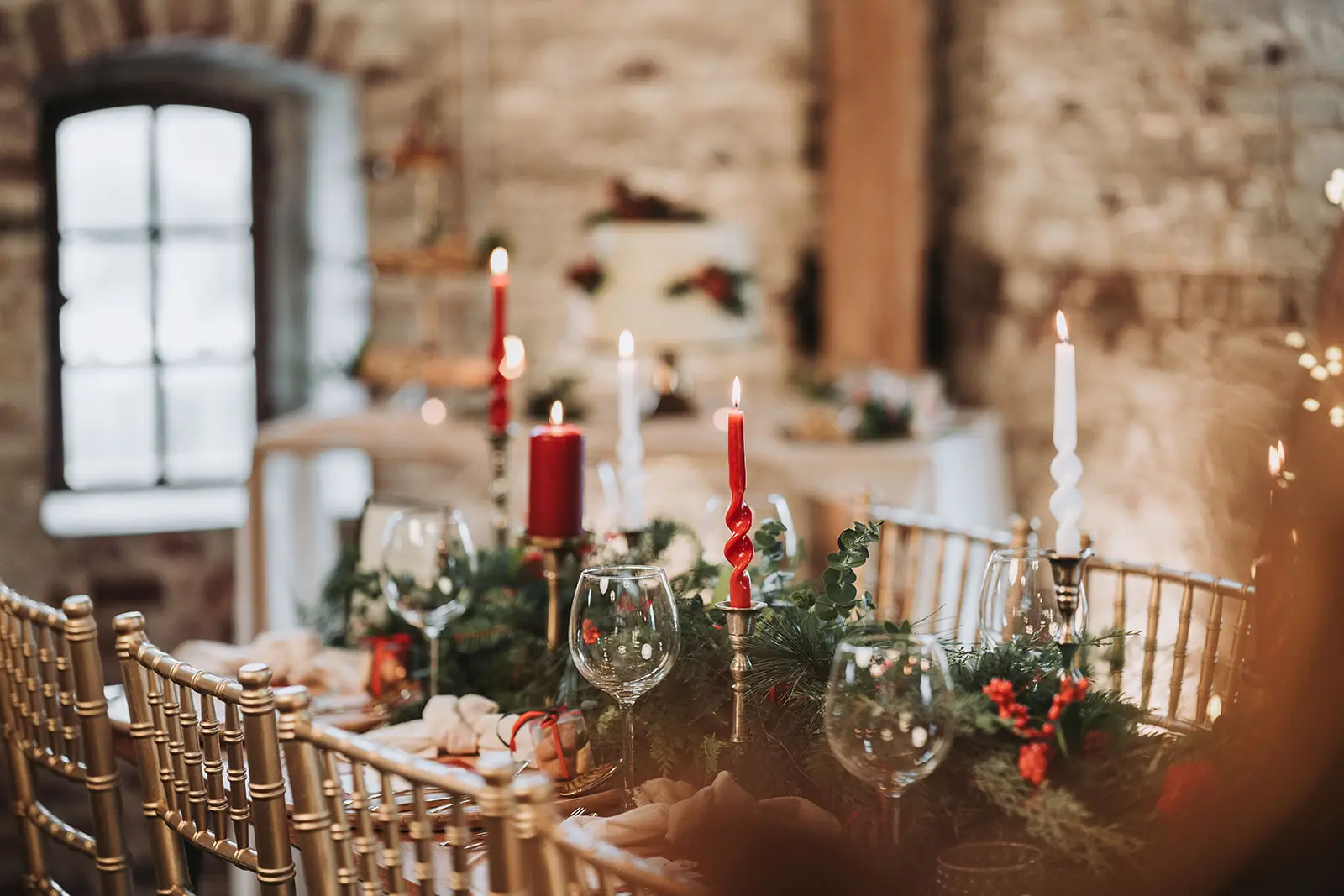 Hochzeitstisch Winterhochzeit mit roten und weißen Stabkerzen grünen Zweigen und goldenen Stühlen