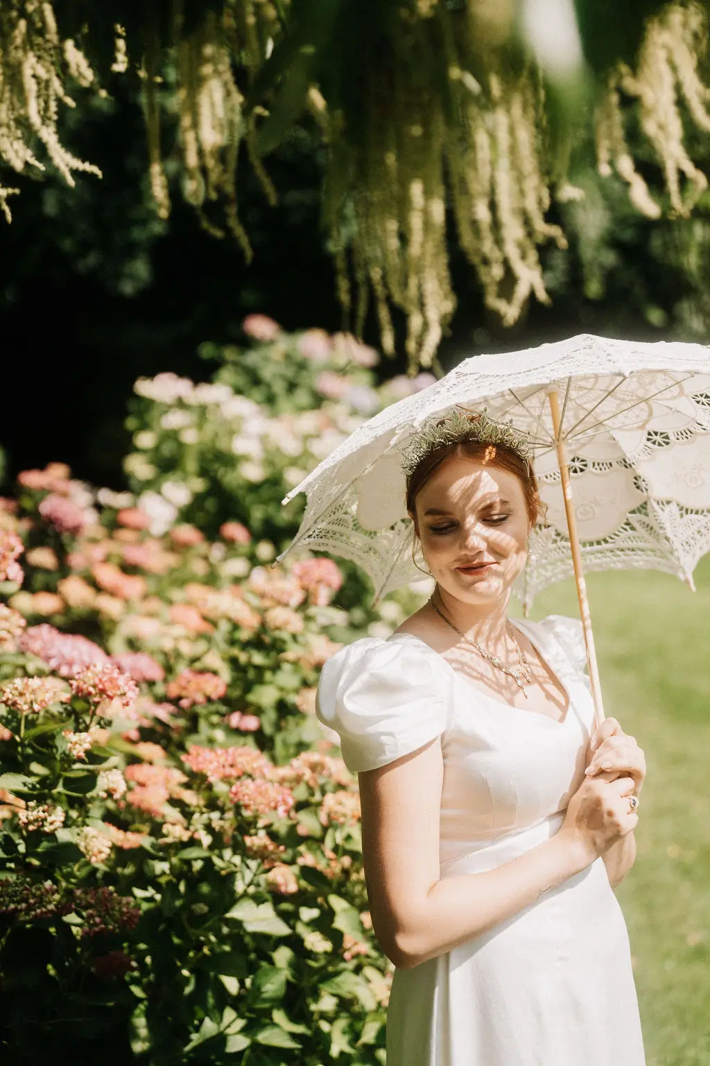 Braut mit Sonnenschirm aus weißer Spitze im Garten