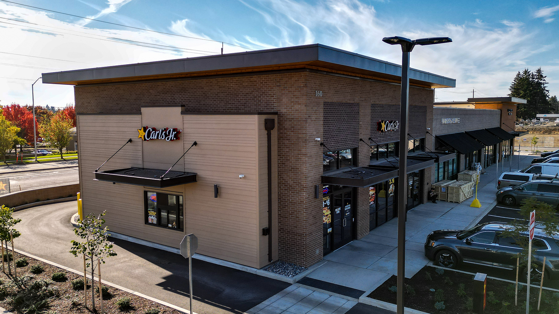 Mid-day aerial photo showing the front corner exterior elevation of Building 3. Installed products include stained cedar 1x6 tight knot tongue and groove used in the parapet enclosed soffit (outdoor ceiling application) and James Hardie® Building Products fiber cement siding of HardiePlank in Select Cedarmill with a staggered reveal of 8in / 4in / 4in / 8 in reveal. Commercial storefront property waterproofing, siding, flashing & soffit installation by StraightLine Exteriors in Camas, Washington 98607. 