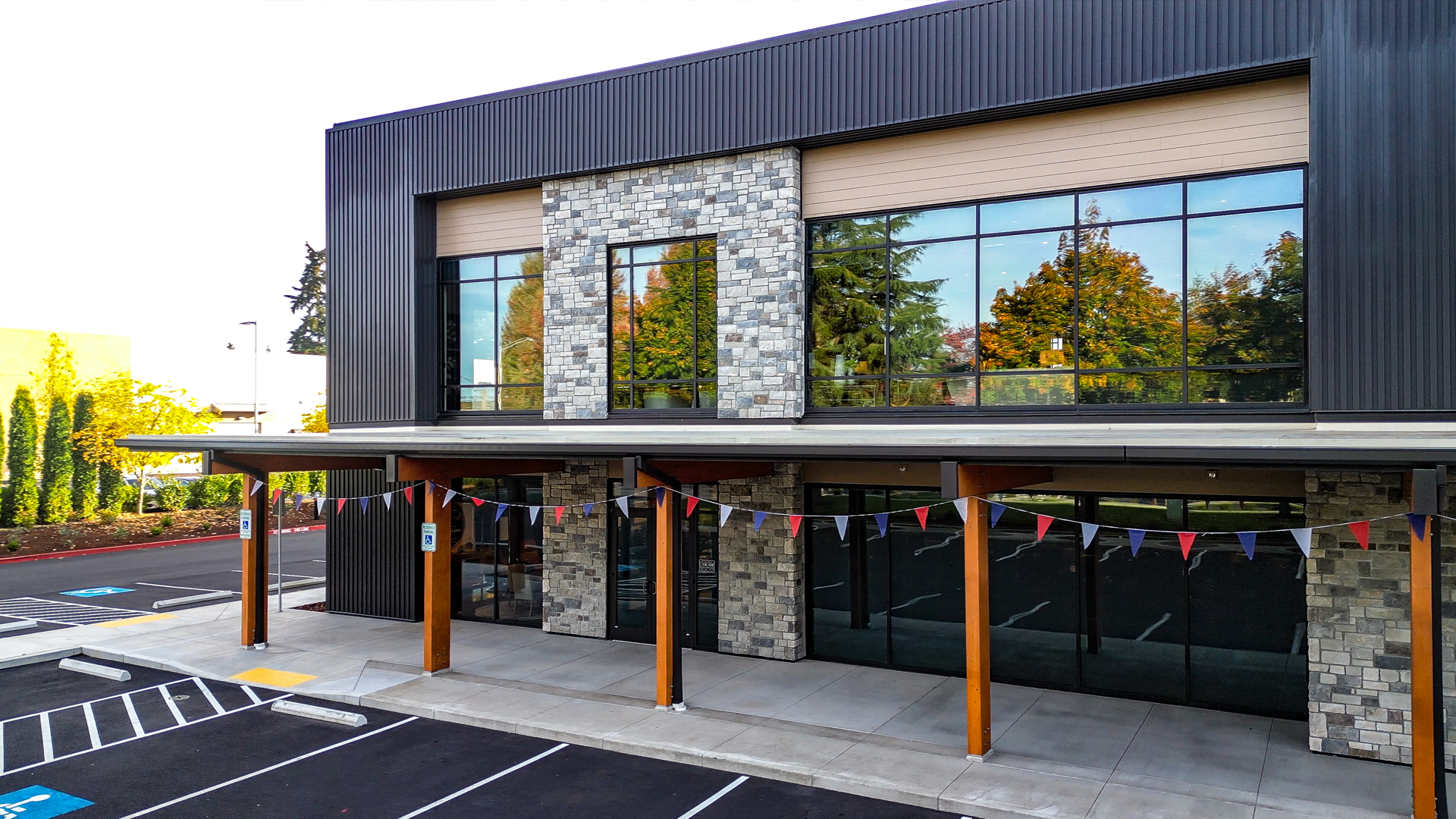 Early morning photography showing the redesigned storefront entryway with black metal siding, tan Hardie®Plank lap siding, stone veneer accents and warm stained cedar wood tones. Photo shows redesigned storefront windows of Cascade Furniture & Mattress after commercial siding, soffit, post & beam installation by StraightLine Exteriors. 