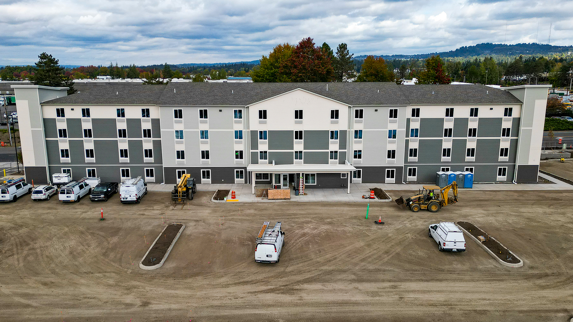 Mid-day aerial photography showing the size, scale and location of WoodSpring Suites Beaverton - Portland West, an extended stay hotel with 122 suites. Traditional residence-style exterior design of WoodSpring Suites Beaverton after commercial waterproofing, siding, window & soffit installation by StraightLine Exteriors in Beaverton, Oregon 97005. © StraightLine Exteriors 