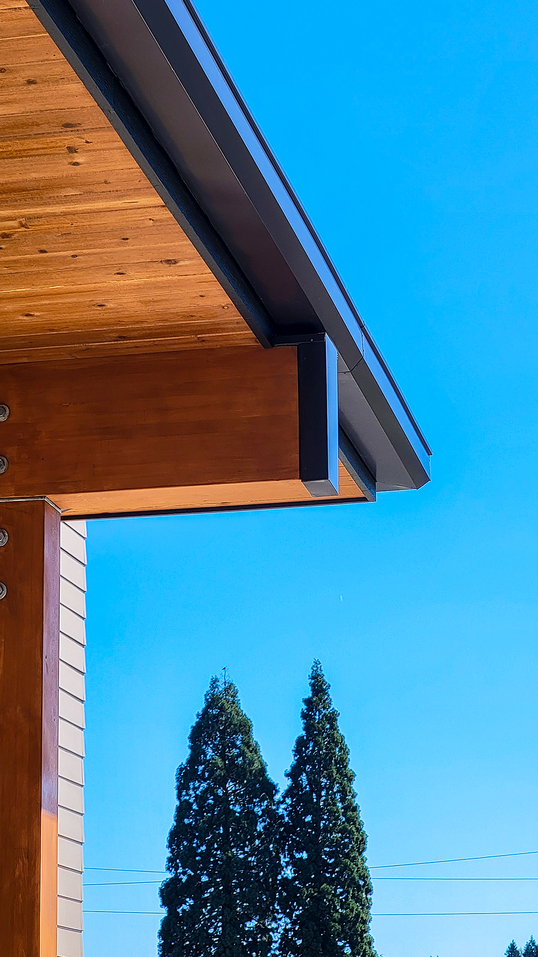 Mid day photography showing the warm wood tones of stained cedar post and beam with black metal flashing cap protection. Modern Industrial design of Cascade Furniture & Mattress after commercial siding, soffit, post & beam installation by StraightLine Exteriors. 