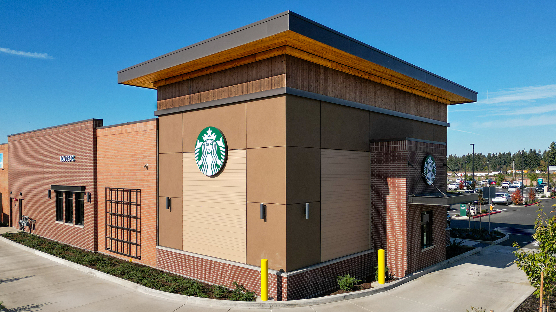 Mid-day aerial photo showing the NE corner elevation of Building 4. Exterior features include stained cedar 1x6 tight knot t & g in the parapet enclosed soffit (outdoor ceiling application) and siding (wall application) of Building 4. Commercial storefront property waterproofing, siding, flashing & soffit installation by StraightLine Exteriors in Camas, Washington 98607. 