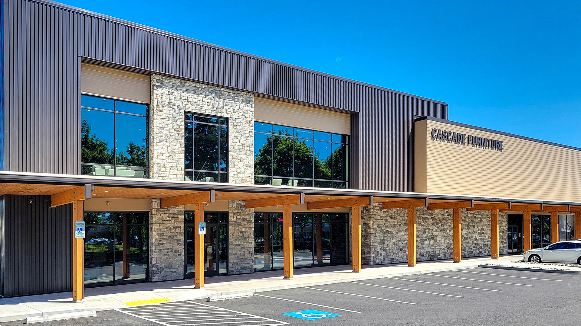 Mid day photography showing the redesigned storefront entryway of Cascade Furniture & Mattress after commercial siding, soffit, post & beam installation by StraightLine Exteriors. 