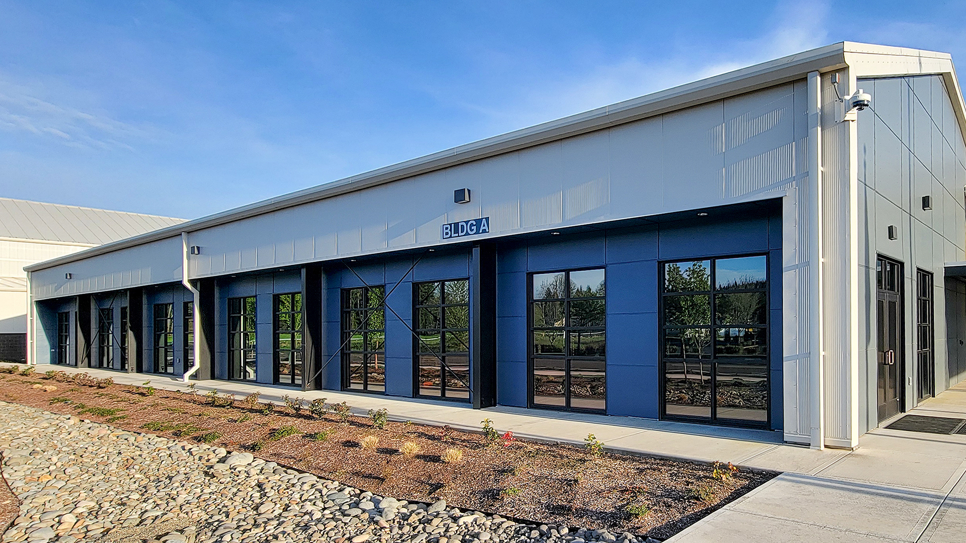 Mid day ground level photograph showing the new Northwest Line Joint Apprenticeship Training Facility (JATC) exterior design and office & classroom exterior elevation. Installed products include James Hardie fiber cement siding Architectural Collection Panels in the texture Fine Sand installed using Tamlyn Architectural Trim & Channel and exposed fasteners. This product was installed by StraightLine Exteriors in Battle Ground, Washington 98604. 