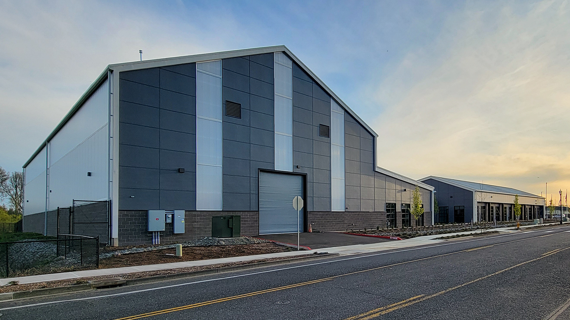 Late day ground level photograph showing the new Northwest Line Joint Apprenticeship Training Facility (JATC) exterior design and rear corner elevation. Installed products include James Hardie fiber cement siding Architectural Collection Panels in the texture Fine Sand installed using Tamlyn Architectural Trim & Channel and exposed fasteners. This product was installed by StraightLine Exteriors in Battle Ground, Washington 98604. 