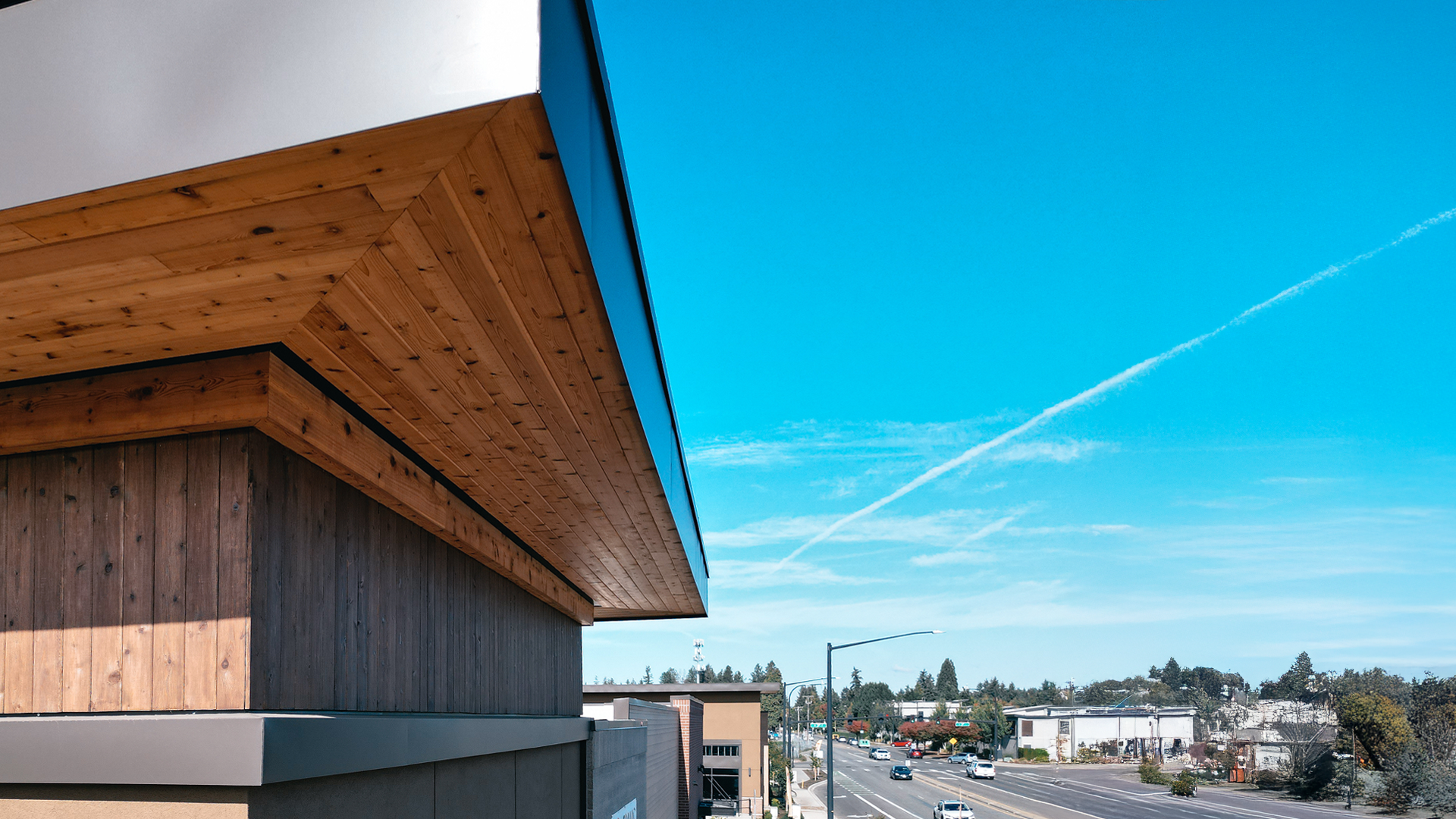 Mid-day aerial photo showing the stained cedar 1x6 tight knot tongue and groove product used in the parapet enclosed soffit (outdoor ceiling application) and siding (wall application) of Building 4. Commercial storefront property waterproofing, siding, flashing & soffit installation by StraightLine Exteriors in Camas, Washington 98607. 