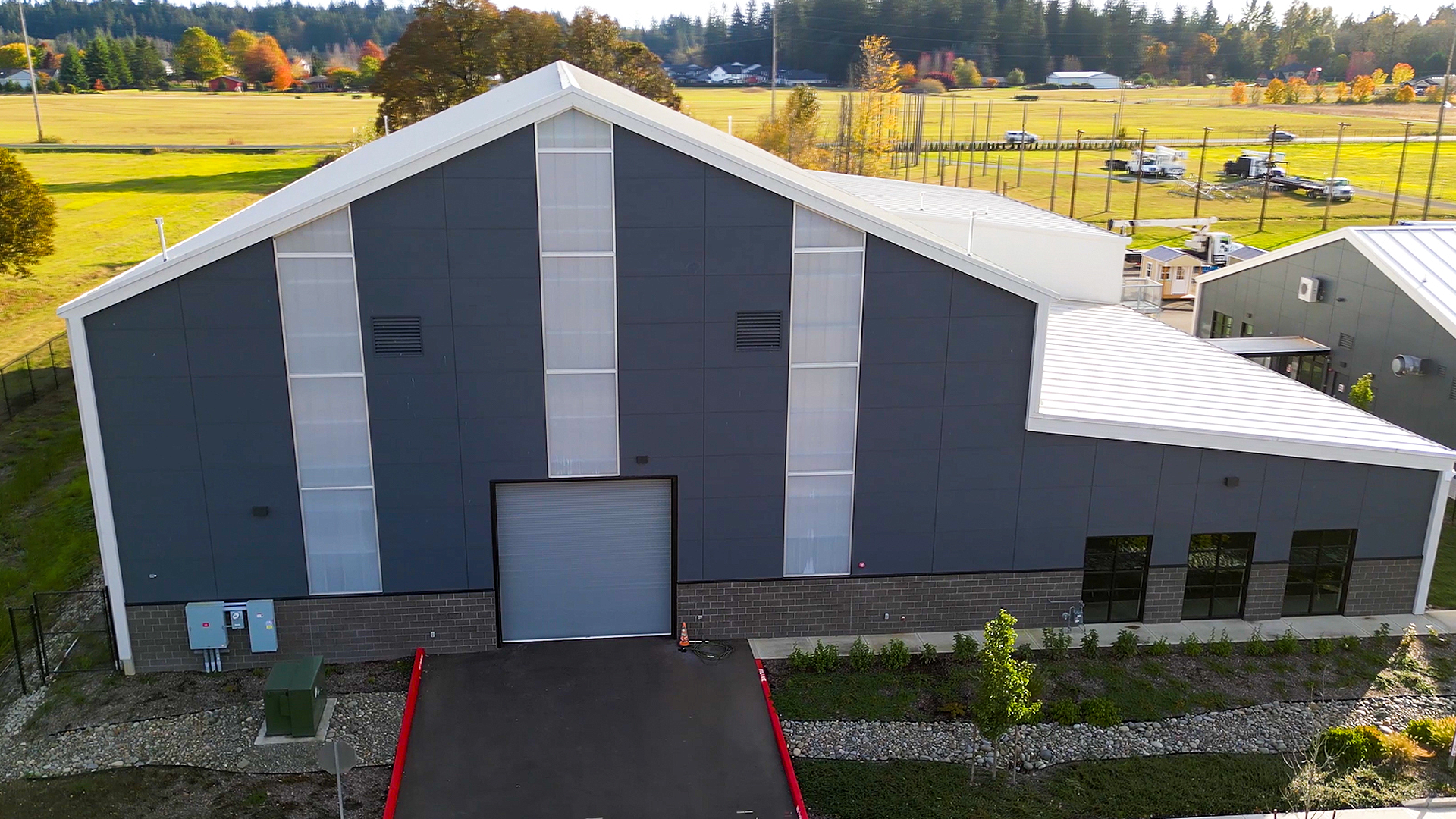 Mid day aerial photograph showing the new Northwest Line Joint Apprenticeship Training Facility (JATC) exterior design and rear training facility elevation. Installed products include James Hardie fiber cement siding Architectural Collection Panels in the texture Fine Sand installed using Tamlyn Architectural Trim & Channel and exposed fasteners. This product was installed by StraightLine Exteriors in Battle Ground, Washington 98604. 