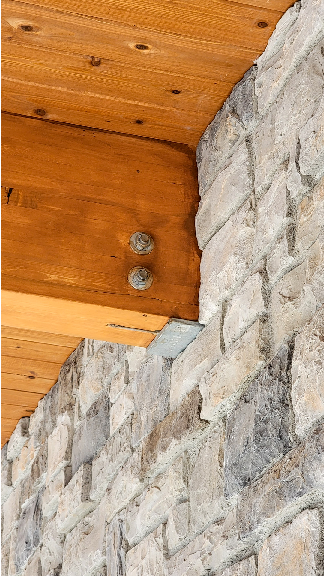 Mid afternoon photography showing the bracket and trim connection of stained cedar beams on stone veneer. Photo of Cascade Furniture & Mattress after commercial siding, soffit, post & beam installation by StraightLine Exteriors. 