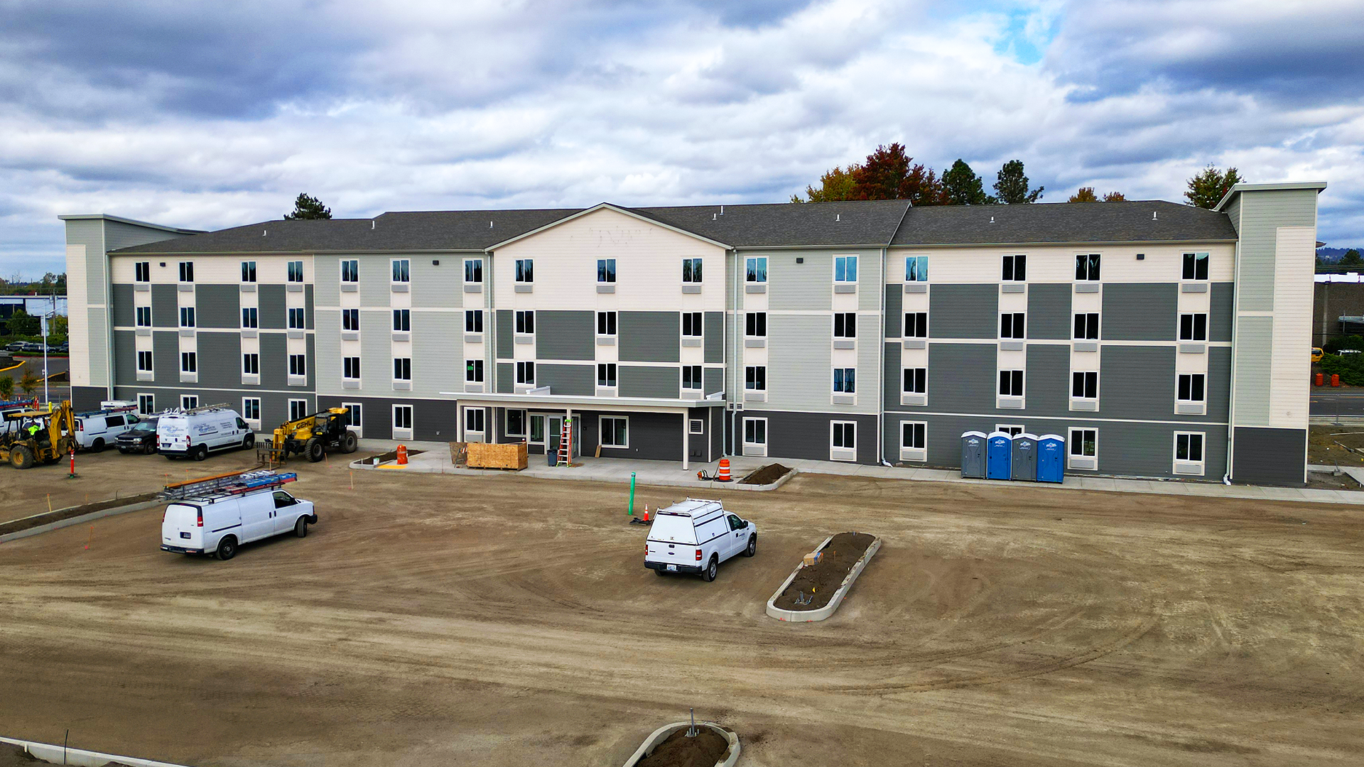 Mid-day aerial photography showing the size, scale and location of WoodSpring Suites Beaverton - Portland West, an extended stay hotel with 122 suites. Traditional residence-style exterior design of WoodSpring Suites Beaverton after commercial waterproofing, siding, window & soffit installation by StraightLine Exteriors in Beaverton, Oregon 97005. © StraightLine Exteriors 