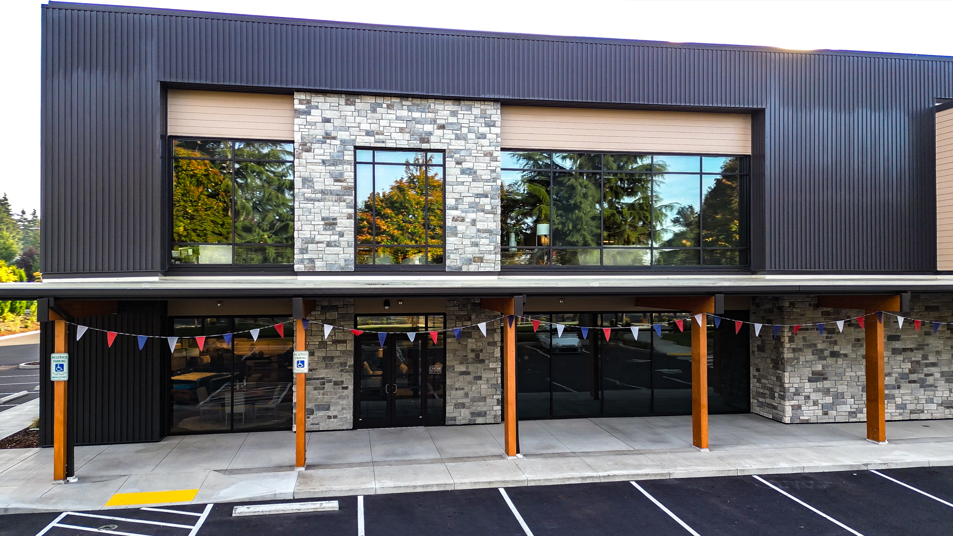 Early morning photography showing the redesigned storefront entryway with black metal siding, tan Hardie®Plank lap siding, stone veneer accents and warm stained cedar wood tones. Photo shows redesigned storefront windows of Cascade Furniture & Mattress after commercial siding, soffit, post & beam installation by StraightLine Exteriors. 