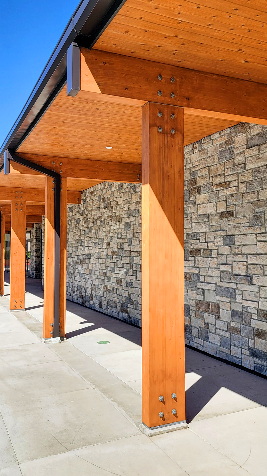 Mid day photography showing the covered walkway and stained cedar post and beam of Cascade Furniture & Mattress after commercial siding, soffit, post & beam installation by StraightLine Exteriors. 