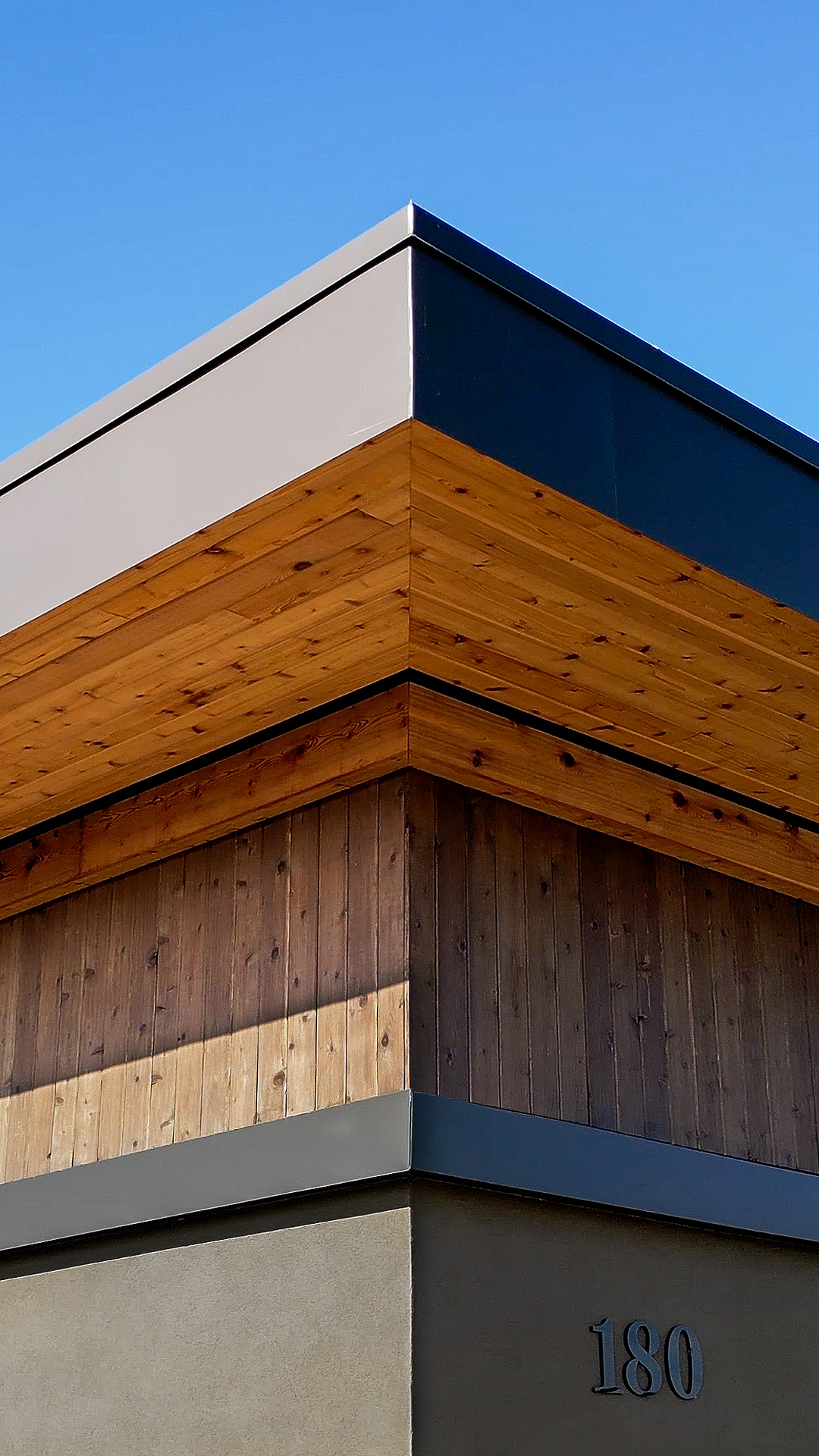 Up-close, mid-day aerial photo showing the stained cedar 1x6 tight knot tongue and groove product used in the parapet enclosed soffit (outdoor ceiling application) and siding (wall application) of Buildings 4 & 5. Top of photo also highlights the Stained Cedar Tight Knot Beam Wrap. Commercial storefront property waterproofing, siding, flashing & soffit installation by StraightLine Exteriors in Camas, Washington 98607.