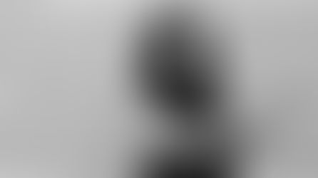 Black-and-white portrait of a confident woman with long, styled hair and glasses, standing against a brick wall with arms crossed. She wears a sleeveless dark top, showcasing forearm tattoos, and gazes directly at the camera, conveying strength and professionalism.