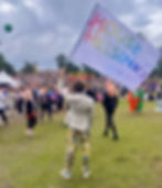 A person facing away from the camera is standing at the pride picnic with a rainbow House of Helsinki flag