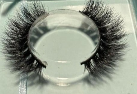 False eyelashes on a clear stand against a light blue background. The lashes are dense and dark, casting shadows. No text visible.