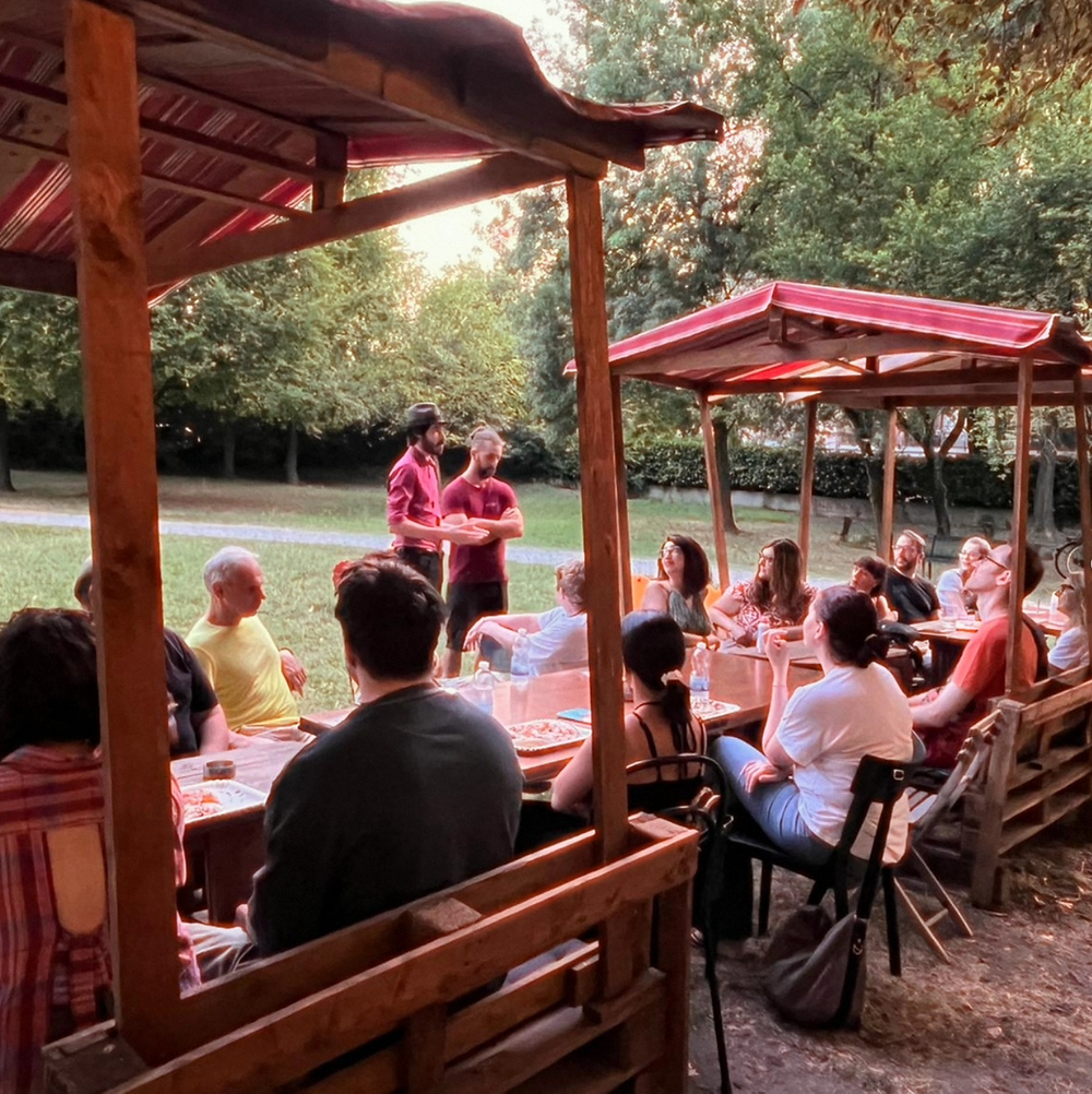 Gruppo di persone a cena all'aperto sotto gazebo in legno.