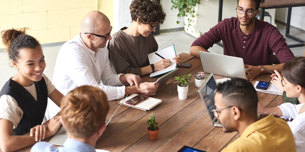 Seven people sat around a wooden table having a meeting.