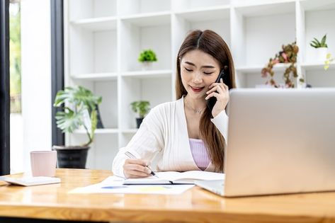 Une femme au téléphone, prend des notes, consulte son agenda. Elle explique qu'elle ne pourra pas participer à une réunion. Son ordinateur est posé devant elle sur un bureau. Elle travaille.