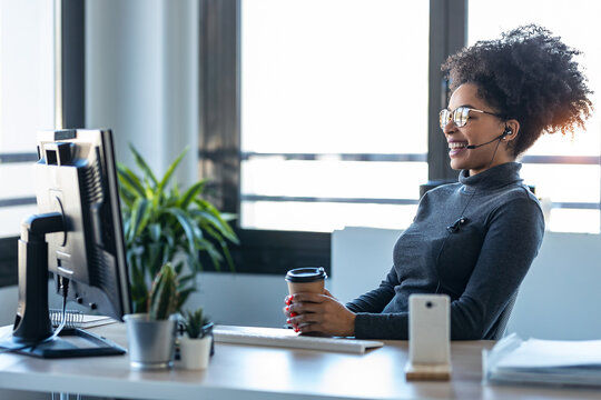 Une femme souriante est assise à son bureau devant un écran. Elle porte un casque et un micro, elle est en visioconférence.