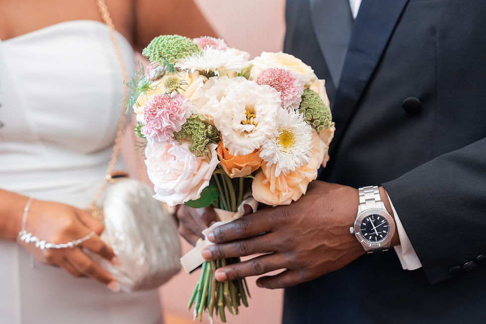 Braut und Bräutigam halten einen pastellfarbenen Blumenstrauß bei einer Hochzeit; elegante Stimmung, dunkler Anzug, weißes Kleid.