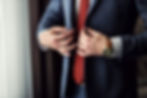 Mann mit roter Krawatte und Uhr knüpft sich den Veston zu.jpg