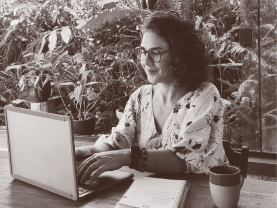 Bela Pagliosa, da Lúdica Web, trabalhando no notebook em um ambiente cercado por plantas, representando o processo de planejamento e criação estratégica de websites.