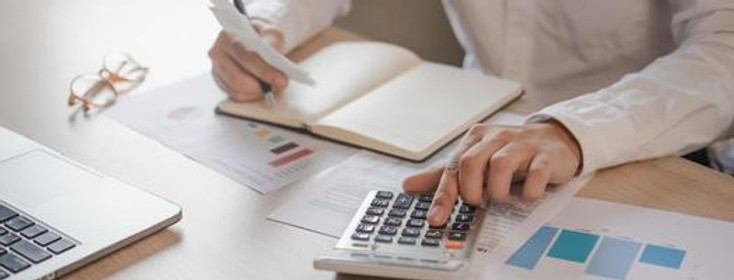 someone writing in a notebook with a calculator