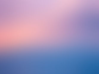 Photograph of a stunning blue, pink and golden clouds with clear skies at the top, above an ocean and with snow-topped mountains far off in the distance. The sea is almost still so that the colours of the sky reflect in it. 