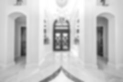 A luxury home entrance, marble floors with great detail, crystal chandelier, opulent door and high ceilings.