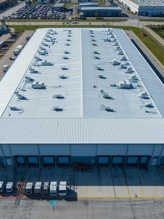 Large industrial building, white flat roof, many vents, loading docks.