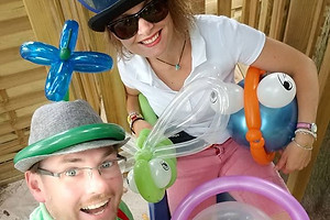 Zwei Ballonkünstler lachen in die Kamera und halten verschiedene Ballonfiguren in den Händen