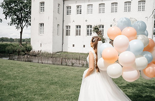 Braut im weißen Brautkleid hält eine Traube pastellfarbender Luftballons