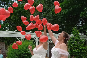 Brautpaar mit in die Luft steigender kleiner roter Herzballons.