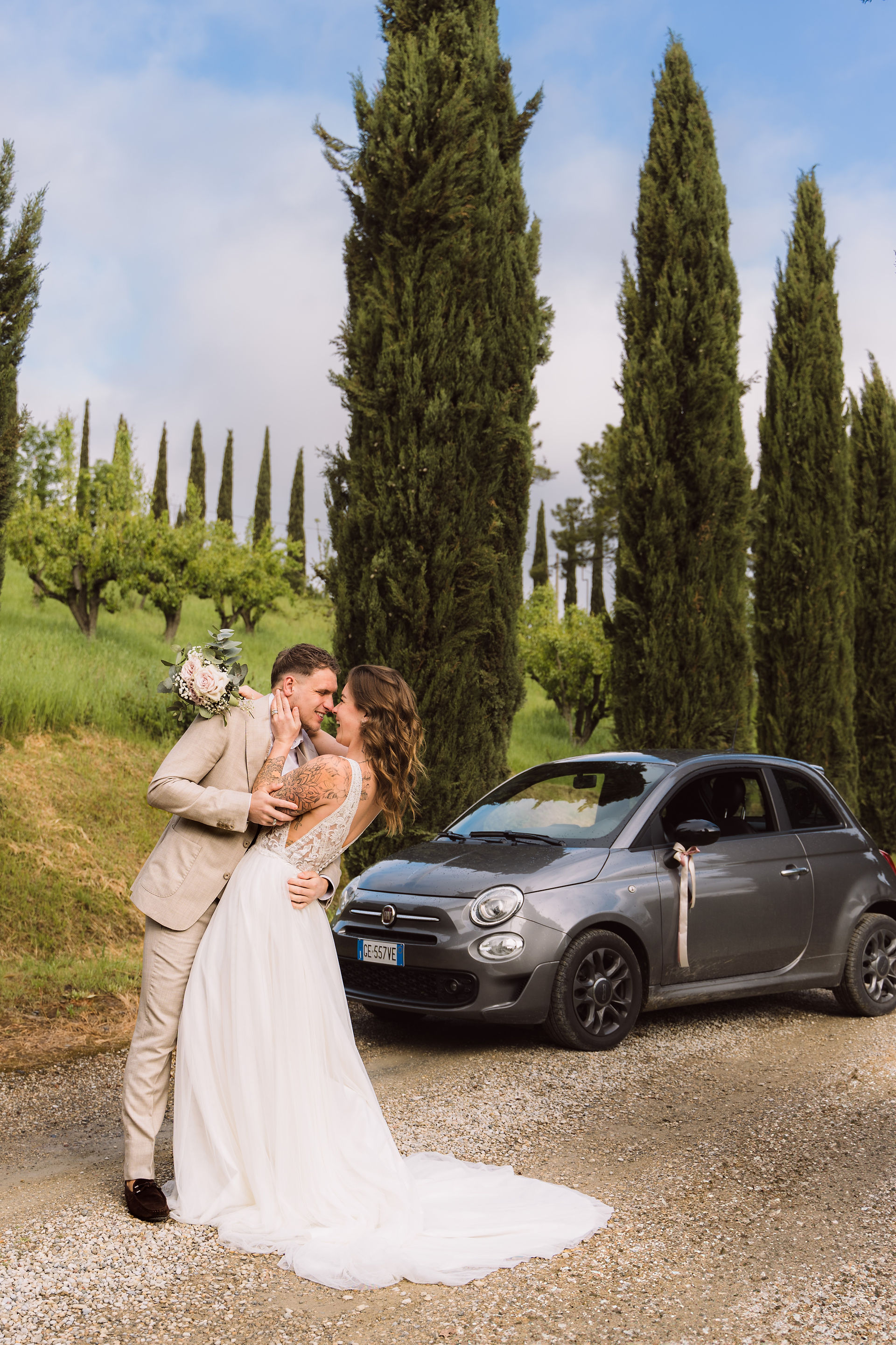 Bruidspaar naast een Fiat 500 bij een cipressenlaan tijdens hun elopement