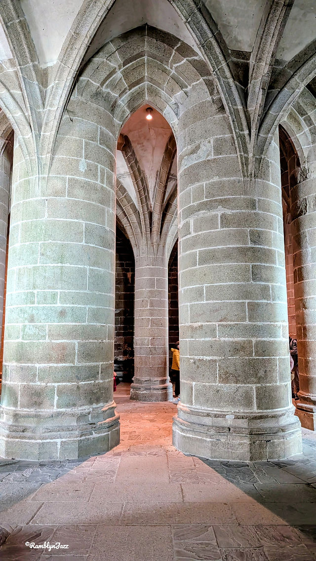 Stone Gothic arches and massive columns inside a cathedral, with a few visitors in the background