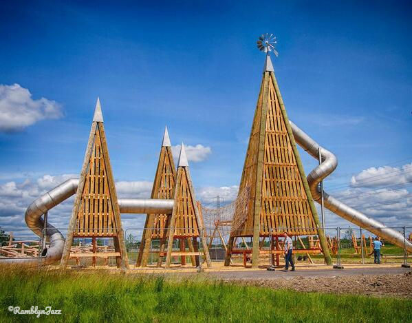 Large wooden pyramid structures with spiral slides in a park under a blue sky.