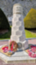 Stone memorial monument with French engravings and wreaths, a Canadian flag, set before a stone wall and trimmed hedges.