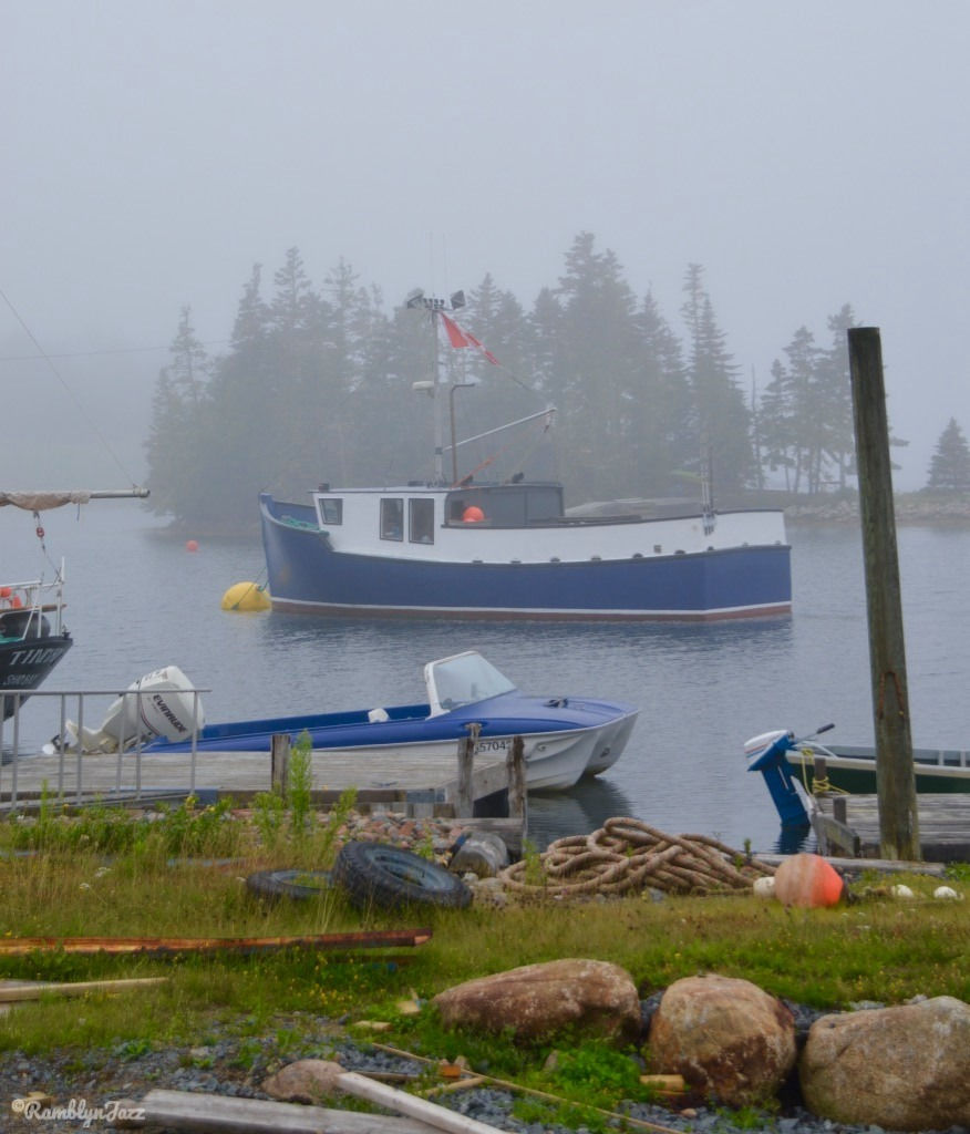 A foggy day with a small fishing boat anchored in ront of a small island. A small speedboat and some fishing bouys ar in the foreground.