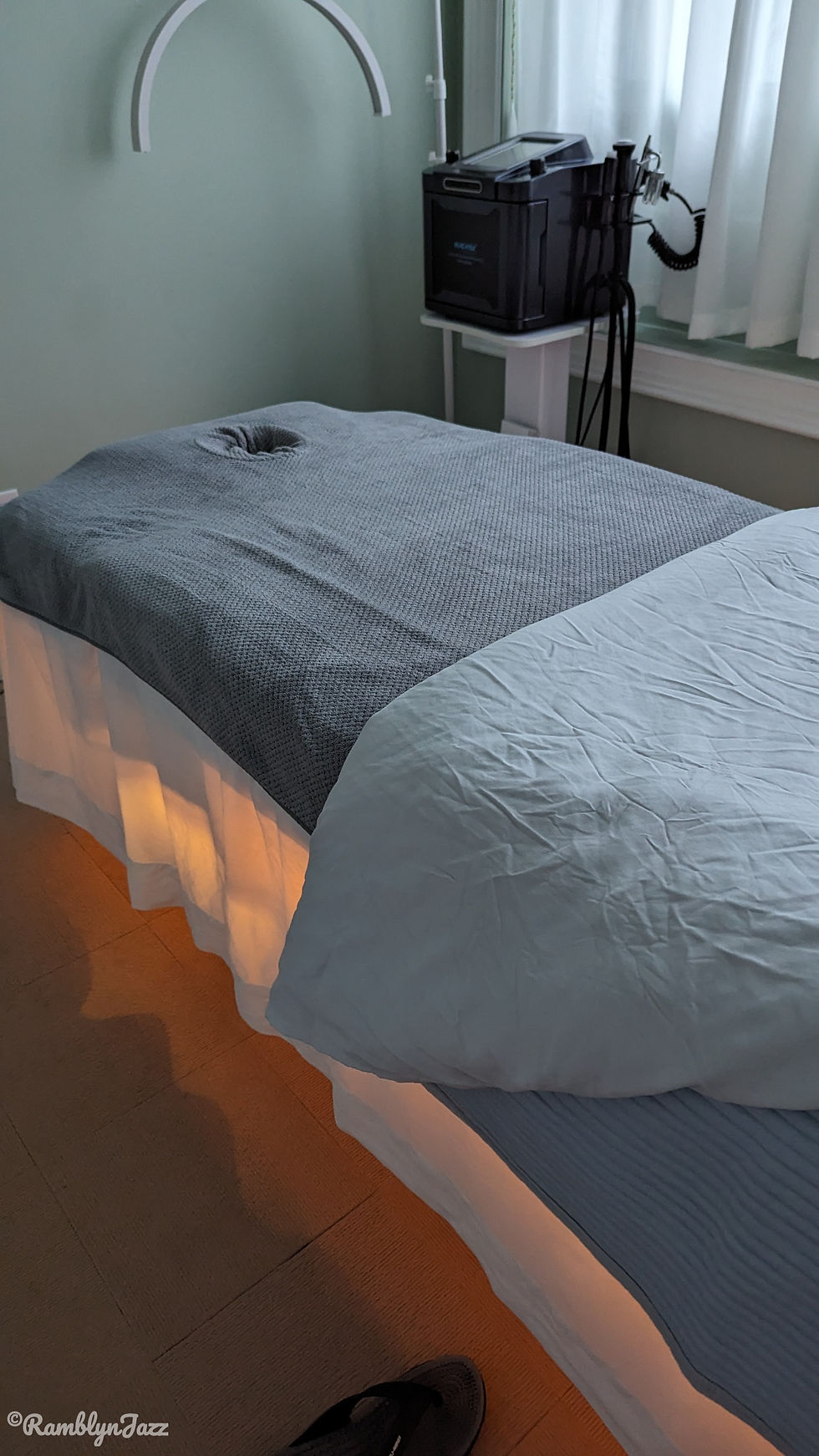 Inside a massage room, looking t the table covered with grey linens