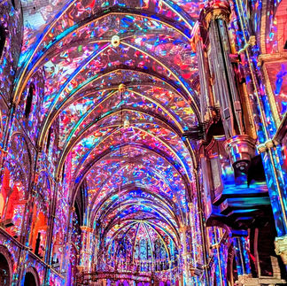 Rainbow lights fill a gothic cathedral interior with vaulted ceilings, a large pipe organ, and glowing arches.