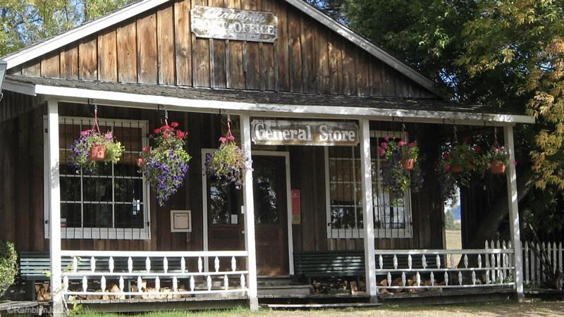 a small wood cabin with a porch ad white railings. planters re hnnging from the porch.sign above the door says 'General Store'