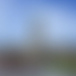 People gather in front of a large historic building with a central clock tower under a blue sky. The scene is lively and vibrant.