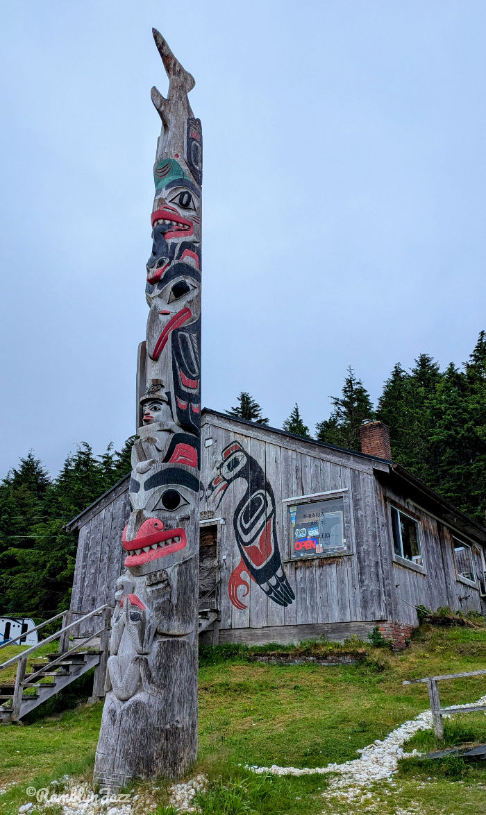 a weathered wooden longhouse style building with Haida art painted on the exterior and a house pole in front