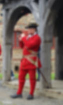 Man in red historical uniform playing a flute under a wooden archway, with stone building in background. Mood is focused and historical.