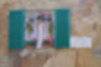 A window on aa stone wall. The window is surrounded by green shutters and has flowers and bird houses displayed on the ledge. Beside the window is a sign "Piazza del Conte"