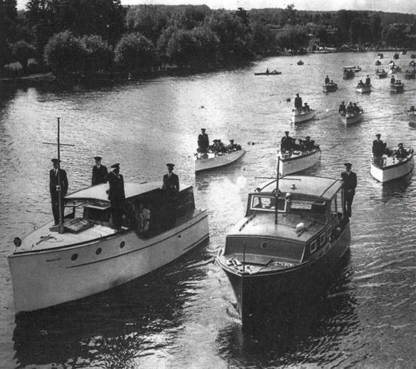 Black-and-white river scene with many small boats and uniformed men on deck, moving along a tree-lined waterway.